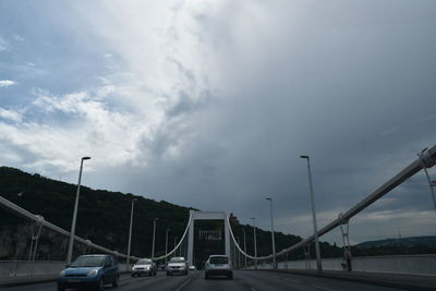 Cars moving on road against cloudy sky