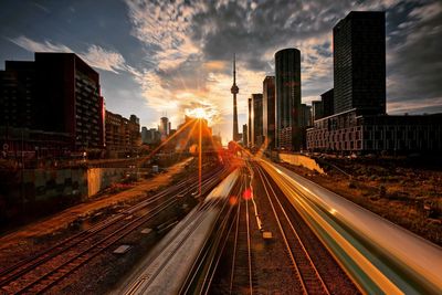 Railroad tracks amidst buildings in city against sky during sunset