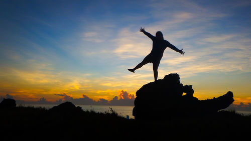 Silhouette man jumping at sea against sky during sunset