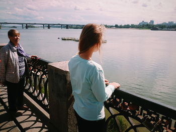 Rear view of woman standing by railing against lake