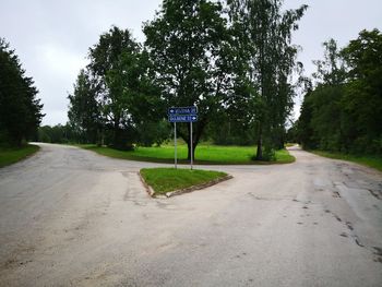 Road sign by trees in city against sky