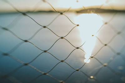Scenic view of sea seen through chainlink fence on sunny day