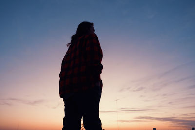 Rear view of woman standing against sky during sunset