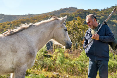 Mature bearded man meeting white horse while hiking in rural pasture. friendship and relationship