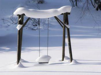 Snow covered swing on field against sky
