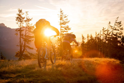 Man riding bicycle on field against sky during sunset