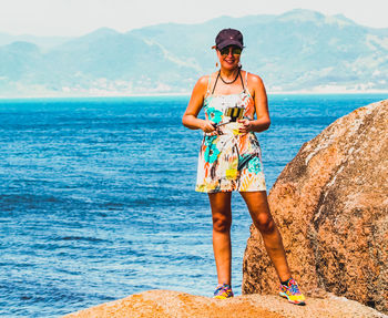 Full length of woman standing on rock against sea