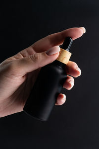 Cropped hand of person holding bottle against black background