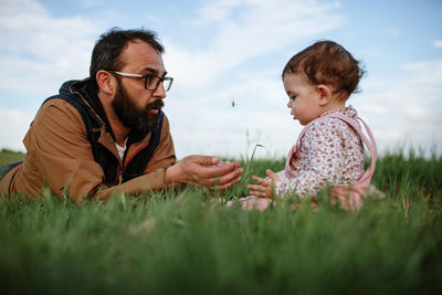 Father and daughter on grass against sky