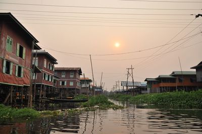 Canal by buildings against sky during sunset