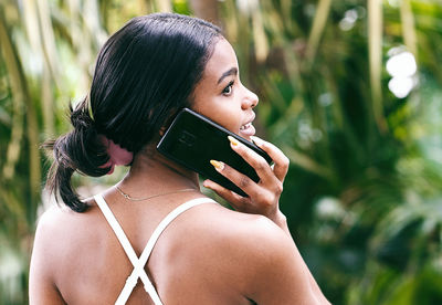 Young woman talking over mobile phone while looking away against plants