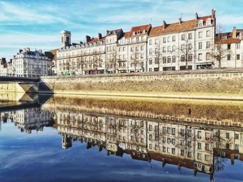 Reflection of buildings on river against sky in city