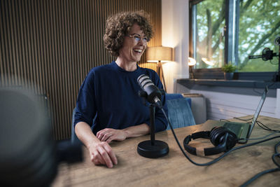 Cheerful radio dj recording podcast through microphone in studio