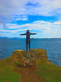 Full length of man standing on rocks by sea against sky