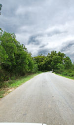 Empty road along trees and plants against sky