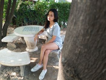 Portrait of young woman sitting on rock against trees