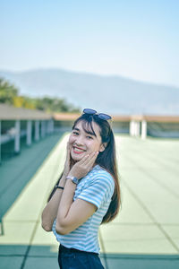 Portrait of smiling young woman standing against sky