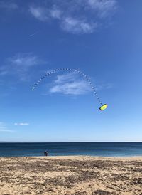 People flying kite while standing at shore of beach against sky