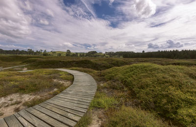 Boardwalk on field against sky