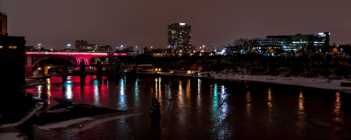 Bridge over river by illuminated buildings at dusk