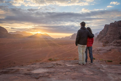 Rear view of couple standing on mountain against sky during sunset