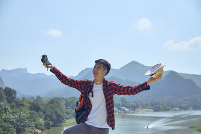 Young man with arms outstretched standing on mountain against sky