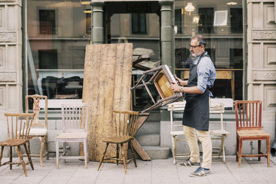 Full length of man holding chair while arranging outside store