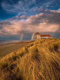 Built structure on beach against sky with rainbow