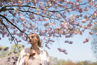 Low angle view of young woman looking at cherry tree