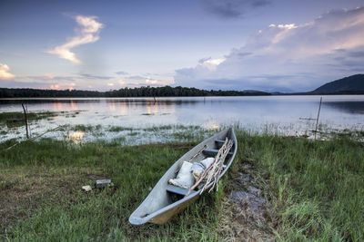 Boat moored at lakeshore against sky during sunset