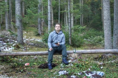 Portrait of man sitting on tree trunk in forest