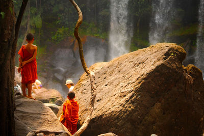 Rear view of monks on rock by waterfall