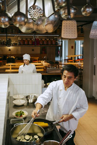 Male chef cooking zucchini with wire whisk in commercial kitchen