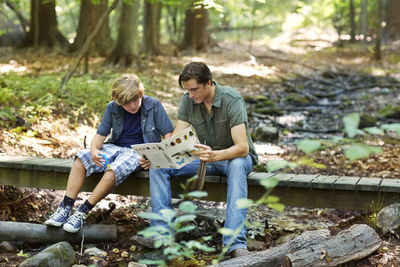 Teacher explaining to student while sitting on footbridge in forest