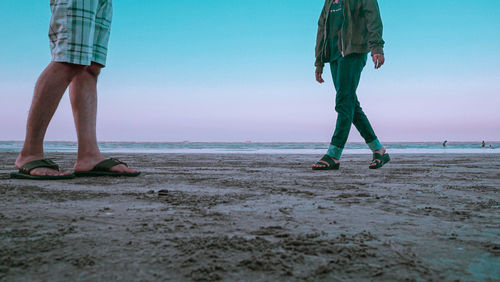 Low section of men on beach against sky