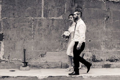 Bride and groom walking on footpath against wall
