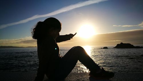 Silhouette boy standing on sea during sunset