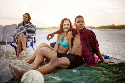 Friends sitting at beach against sky