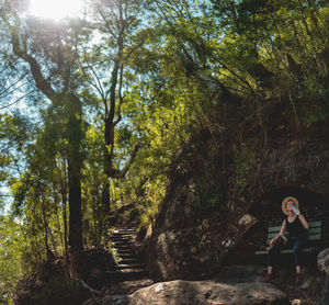 Female hiker sitting on bench against trees at forest