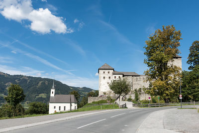 Road by buildings against blue sky in city