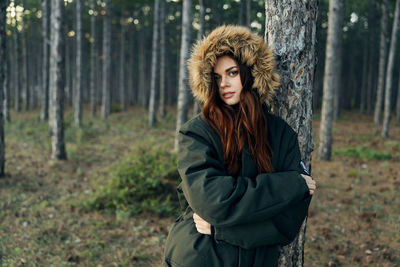 Young woman standing by tree trunk in forest