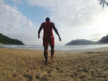 Rear view full length of man walking at beach against sky