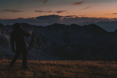 Man photographing on mountain against sky during sunrise