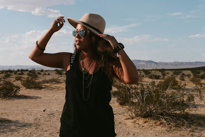 Young woman wearing sunglasses standing on land against sky