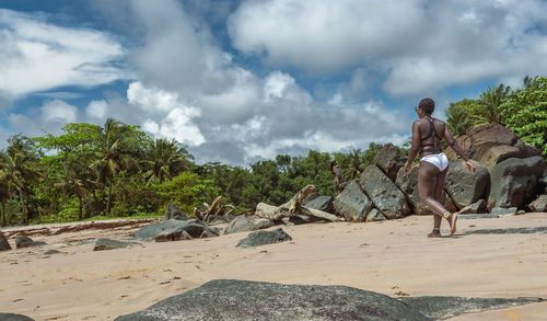 Side view of woman sitting on beach against sky