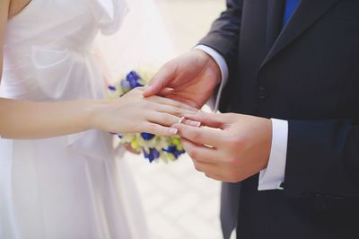 Midsection of bridegroom putting ring in hand of bride 