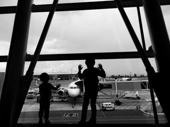 Rear view of children looking through window while standing at airport