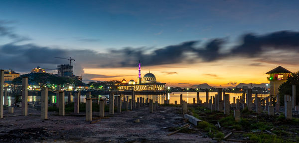 Illuminated buildings at beach against sky during sunset