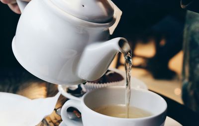 Close-up of teapot pouring drink in cup at table