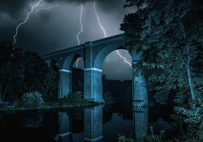 Arch bridge over river against sky at night